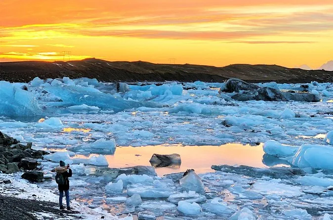 Ein Fotograf am felsigen Ufer von Jökulsárlón bei Sonnenuntergang, die Lagune voller Eis