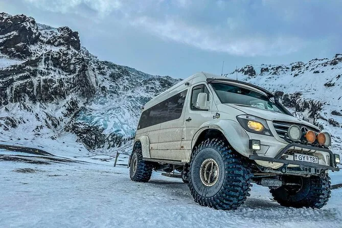 A lifted super jeep with big tyres parked on snow below a dark mountain
