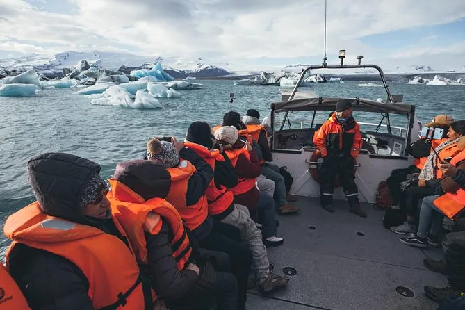 Fahrgäste in orangen Schwimmwesten sitzen auf dem offenen Deck eines Boots und schauen auf Eisberge